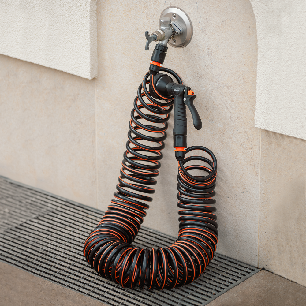 Coiled 10m spiral hose connected to tap with multi-function spray gun, black and orange