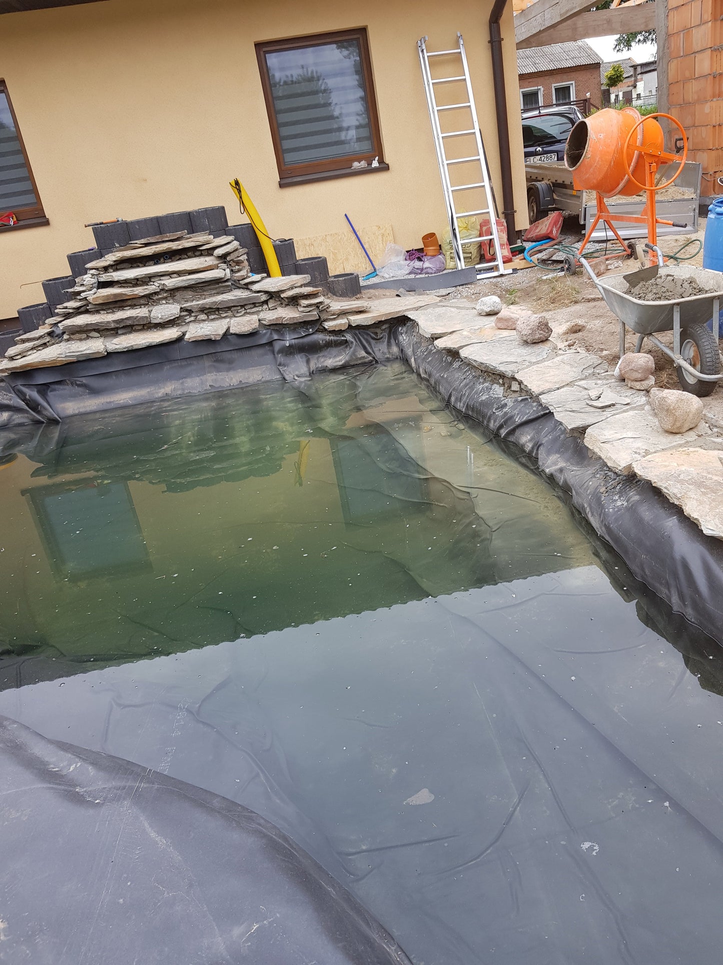 EPDM-Teichliner mit Wasser im Becken, schwarze Folie am Rand um die Steine