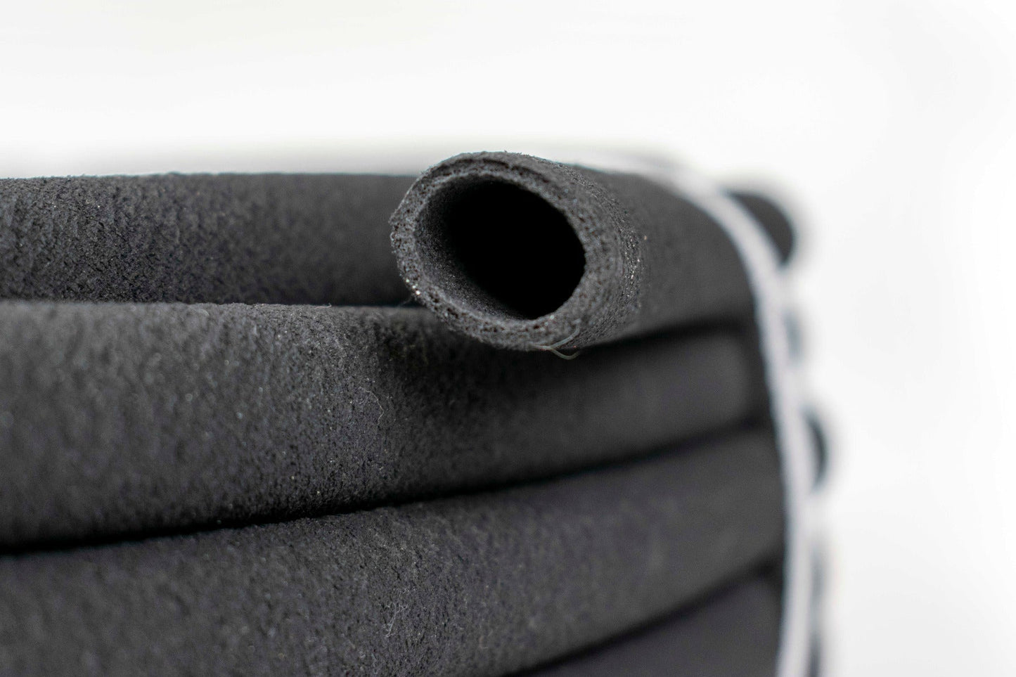 Porous soaker hose end close-up, dark rubber with open porous holes