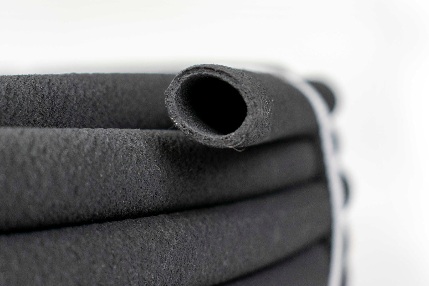 Porous soaker hose end close-up, dark rubber with open porous holes