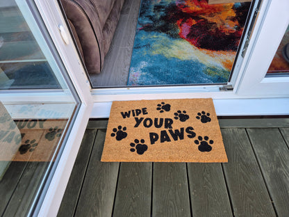 “WIPE YOUR PAWS” coir doormat with black paw prints on wooden porch