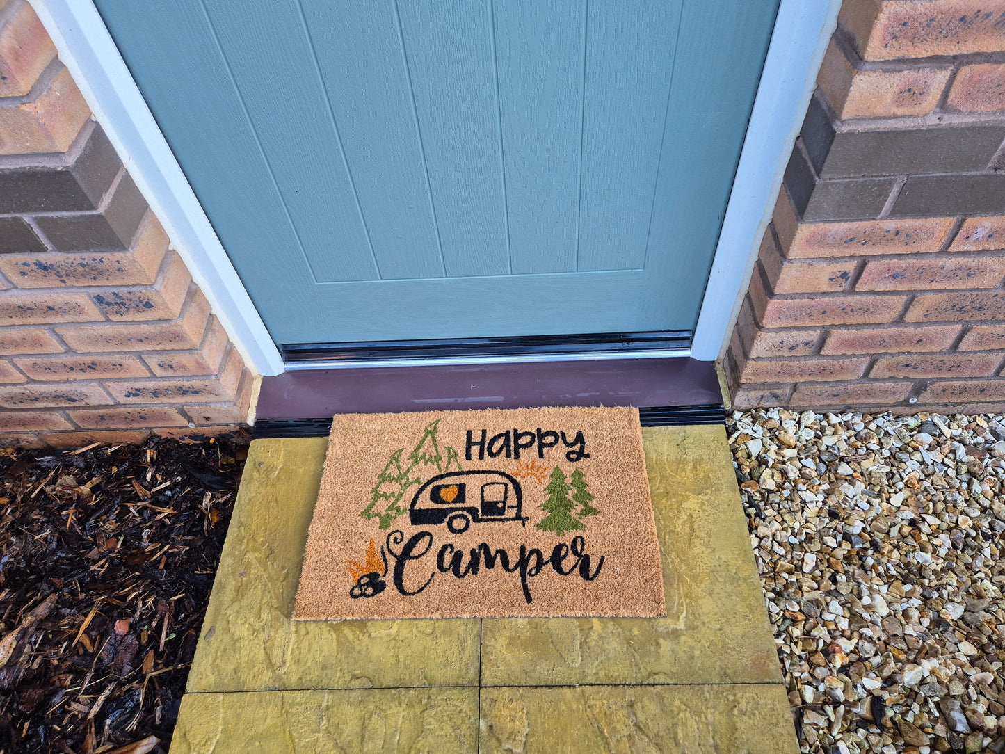 “Happy Camper” doormat on stepping stone walkway, caravan and forest design