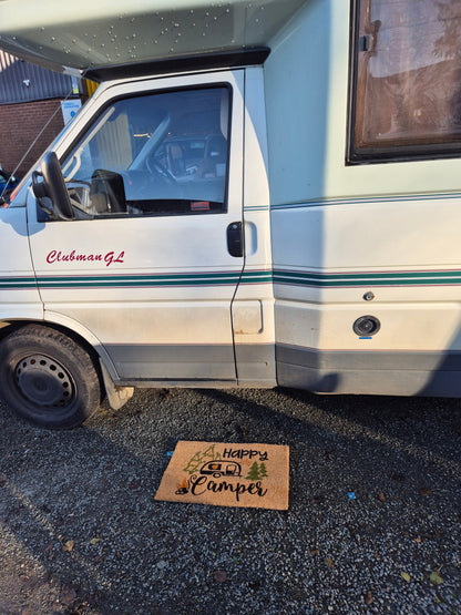 “Happy Camper” doormat laid on driveway beside a van door