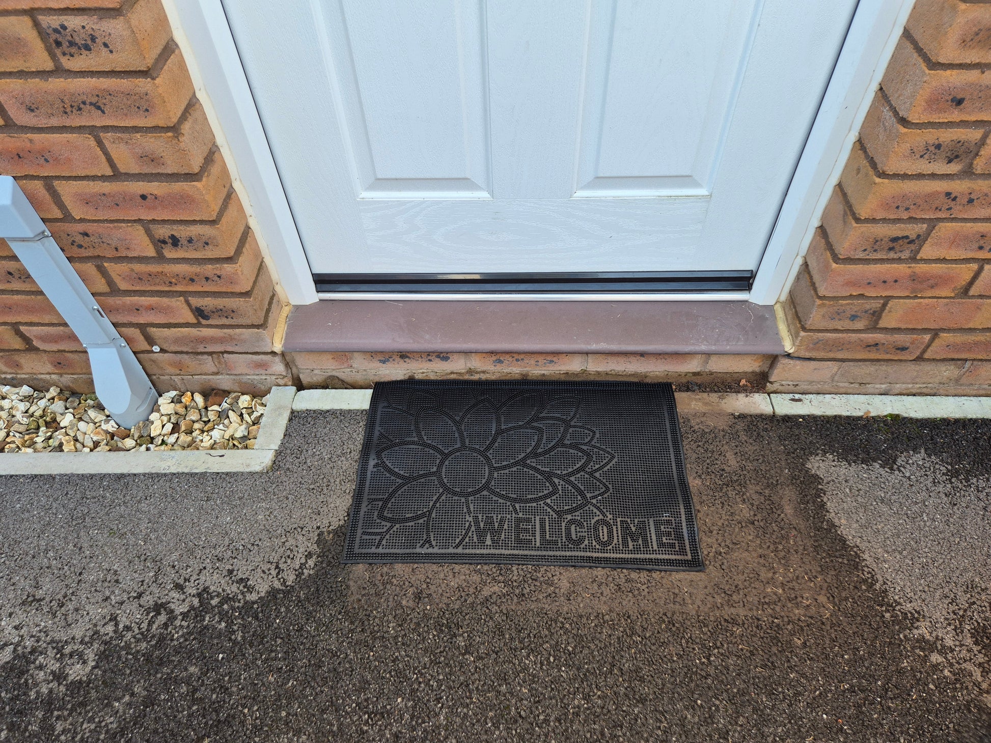 Black 'WELCOME' rubber doormat with flower pattern on doorstep