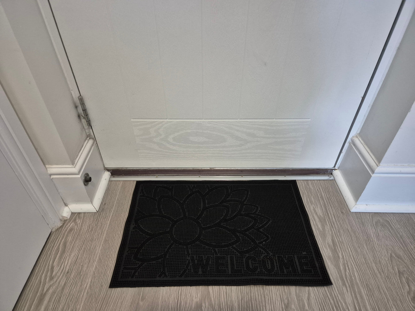 Black rubber doormat with embossed flower and 'WELCOME' inside near door