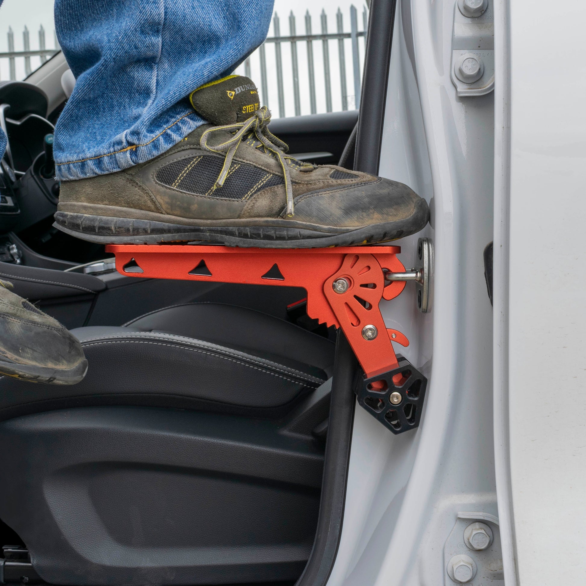 Orange car door step mounted at vehicle door sill, with shoe on black grip strip