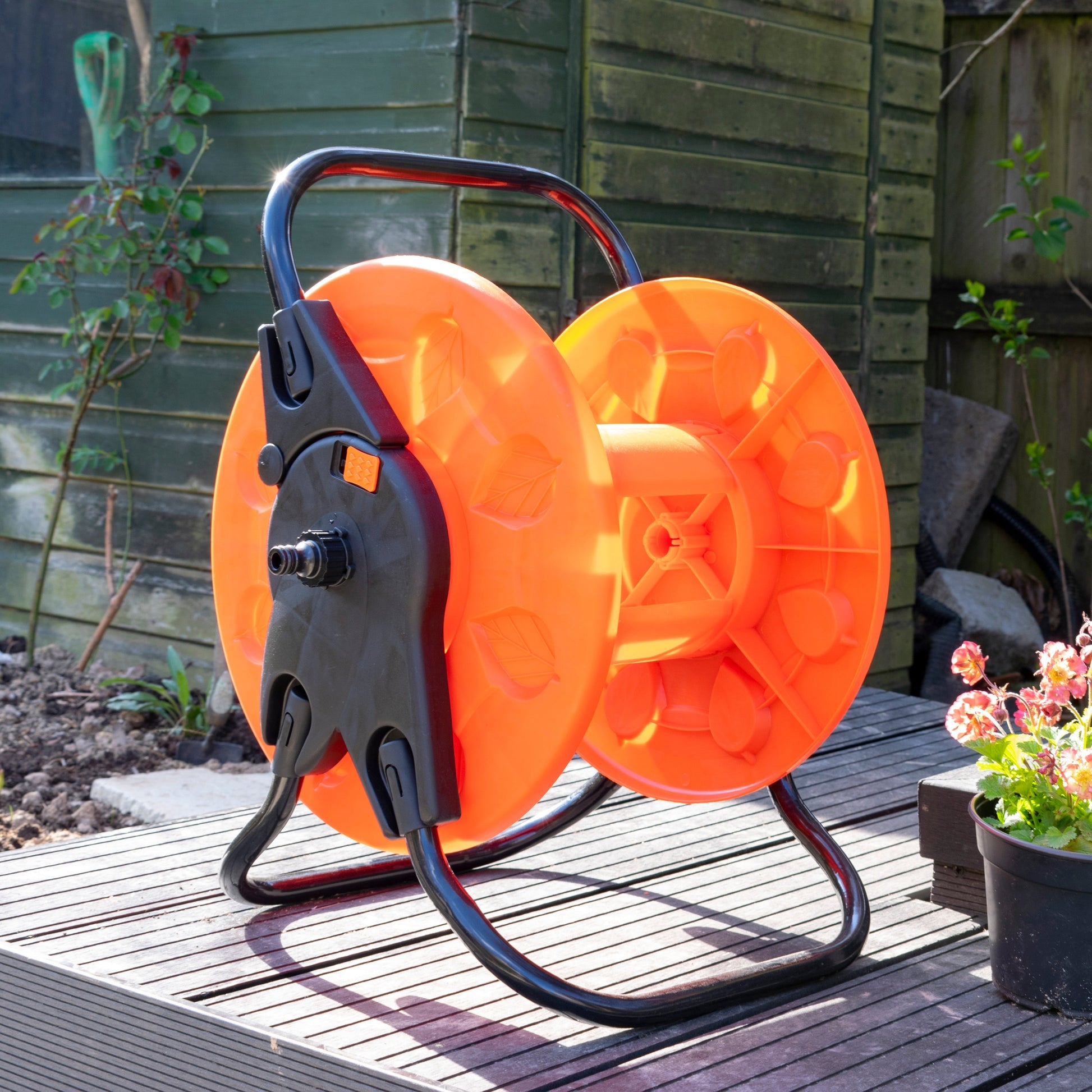 Outdoor garden hose reel cart with orange drum, black housing and curved stand