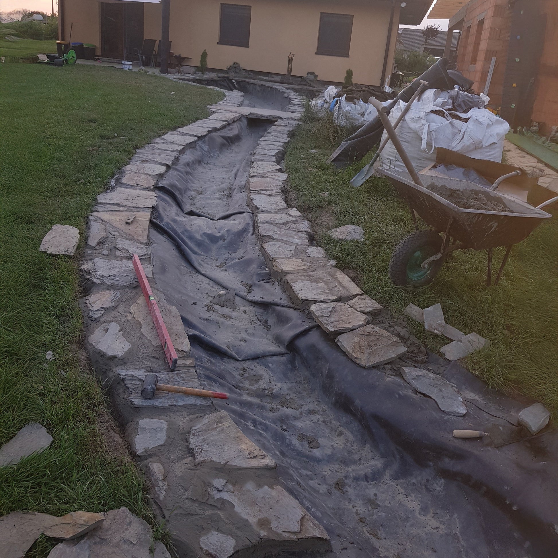 EPDM pond liner with underlay, dark grey membrane lining a rock-edged trench
