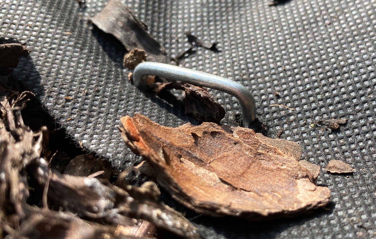 Close-up of galvanized U-shaped weed mat hold down peg on fabric