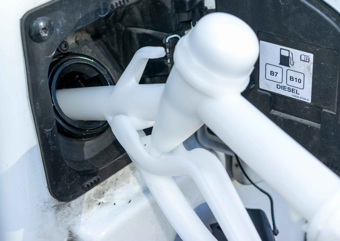 White fuel gun dispensing into fuel filler, visible nozzle and trigger