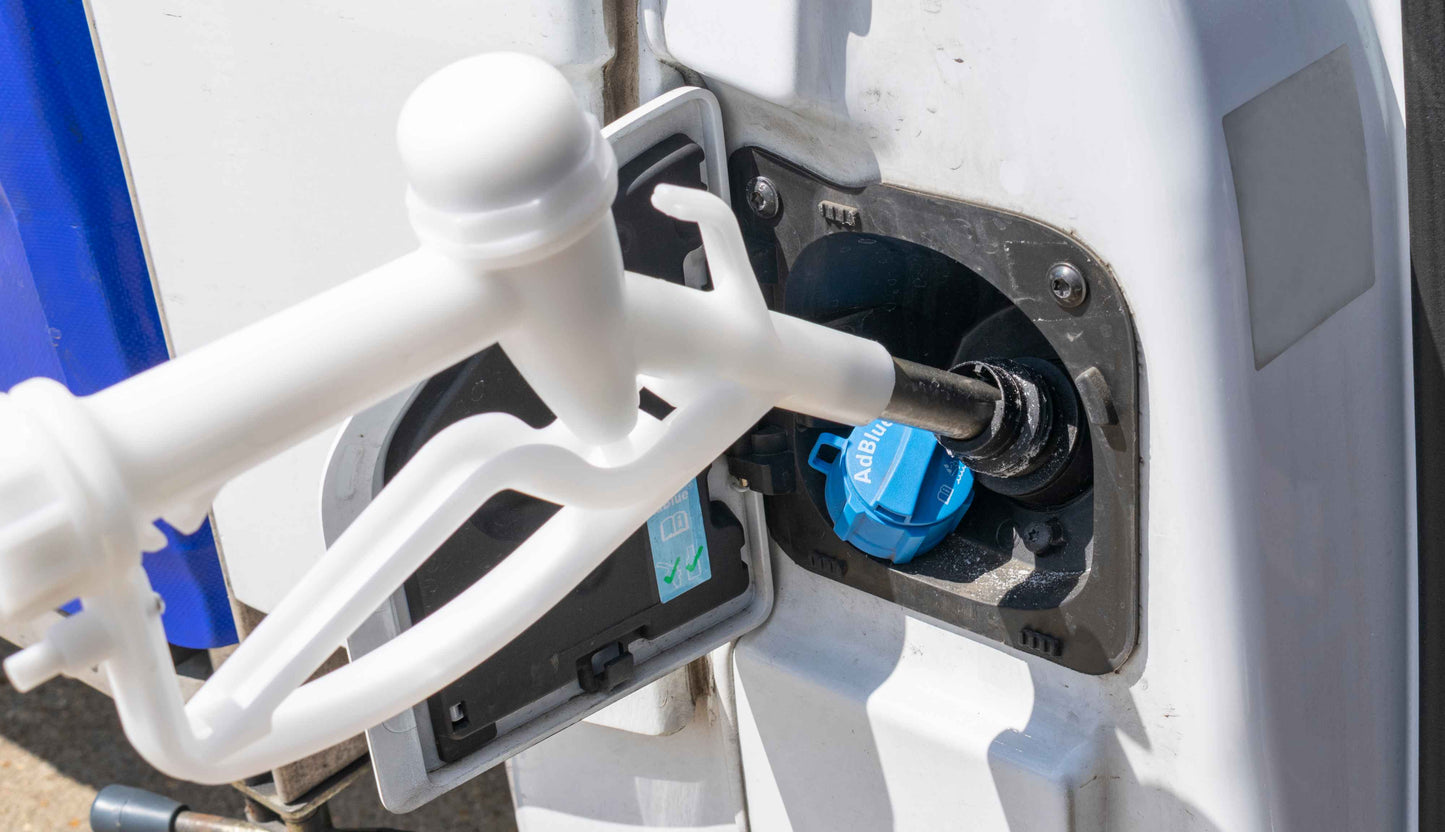 White fuel gun nozzle inserted into vehicle fuel filler, blue cap visible
