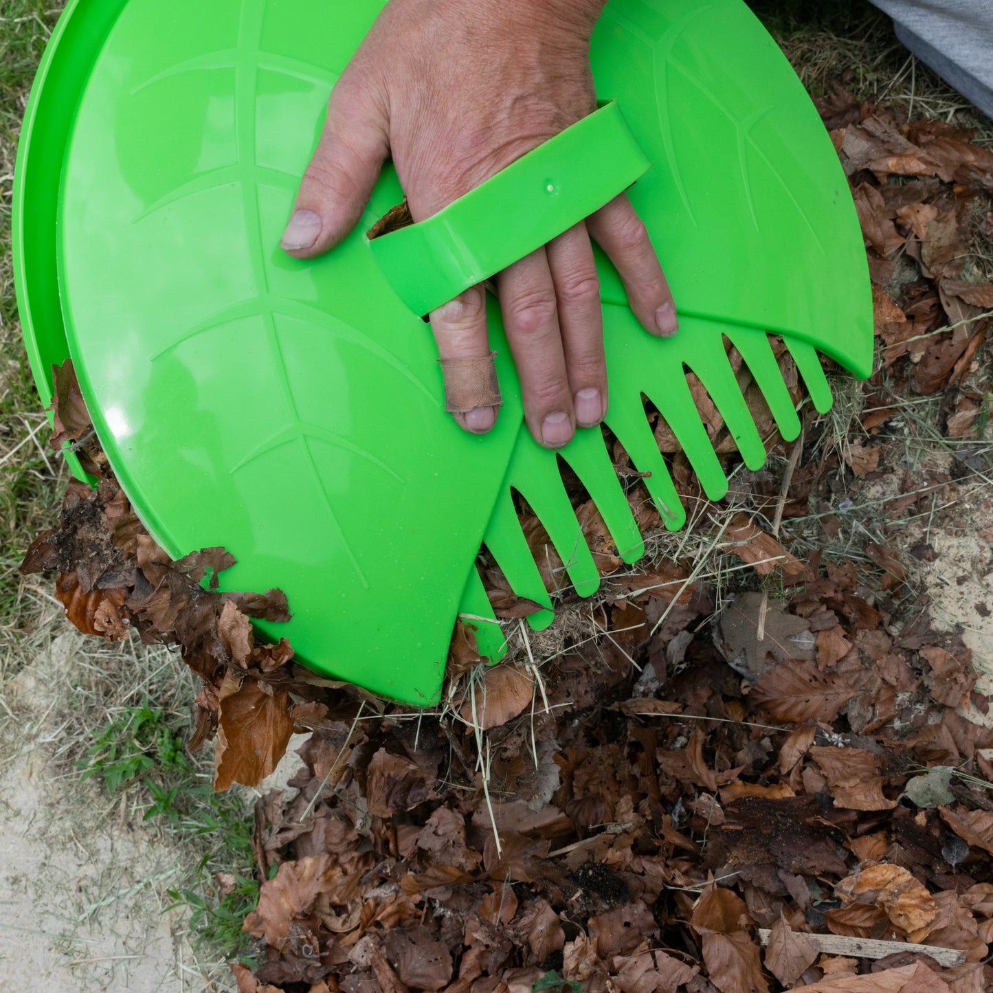 Green leaf grab scoop with wide comb tines, hand grips the leaf-cleaning tool