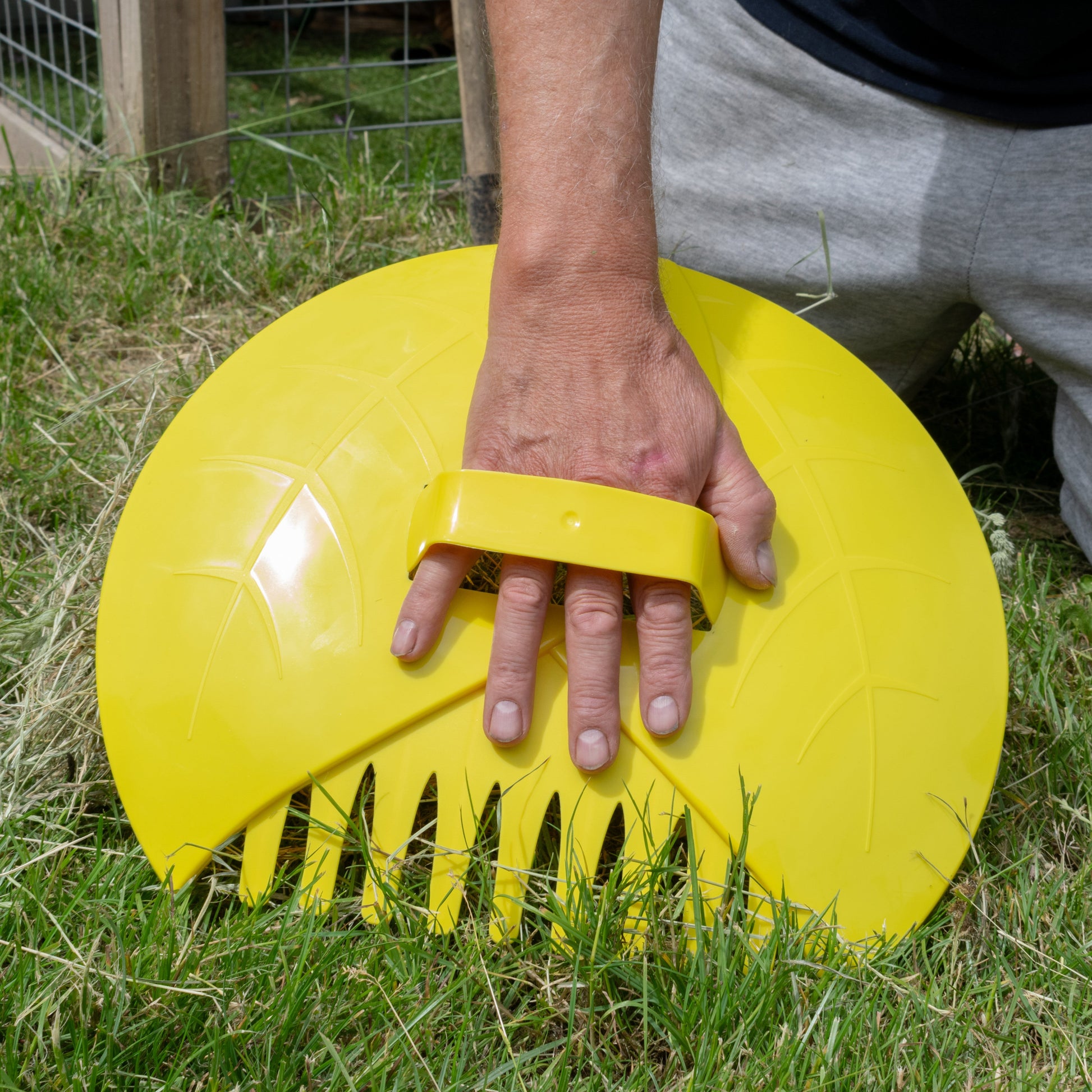 Yellow leaf grabber garden scoop held in hand, showing comb-style teeth