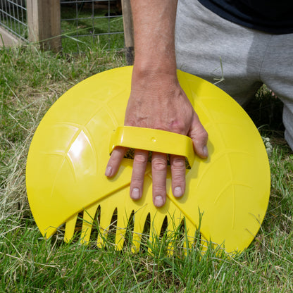 Yellow leaf grabber garden scoop held in hand, showing comb-style teeth