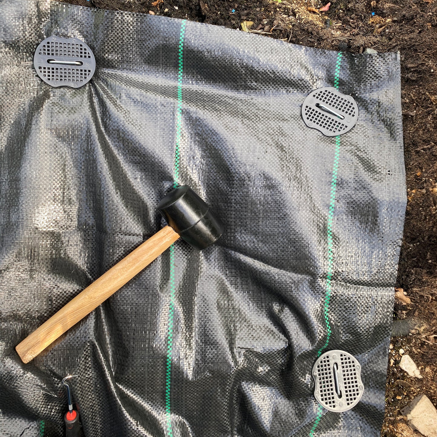 Weed control membrane with securing pegs and rubber mallet on top