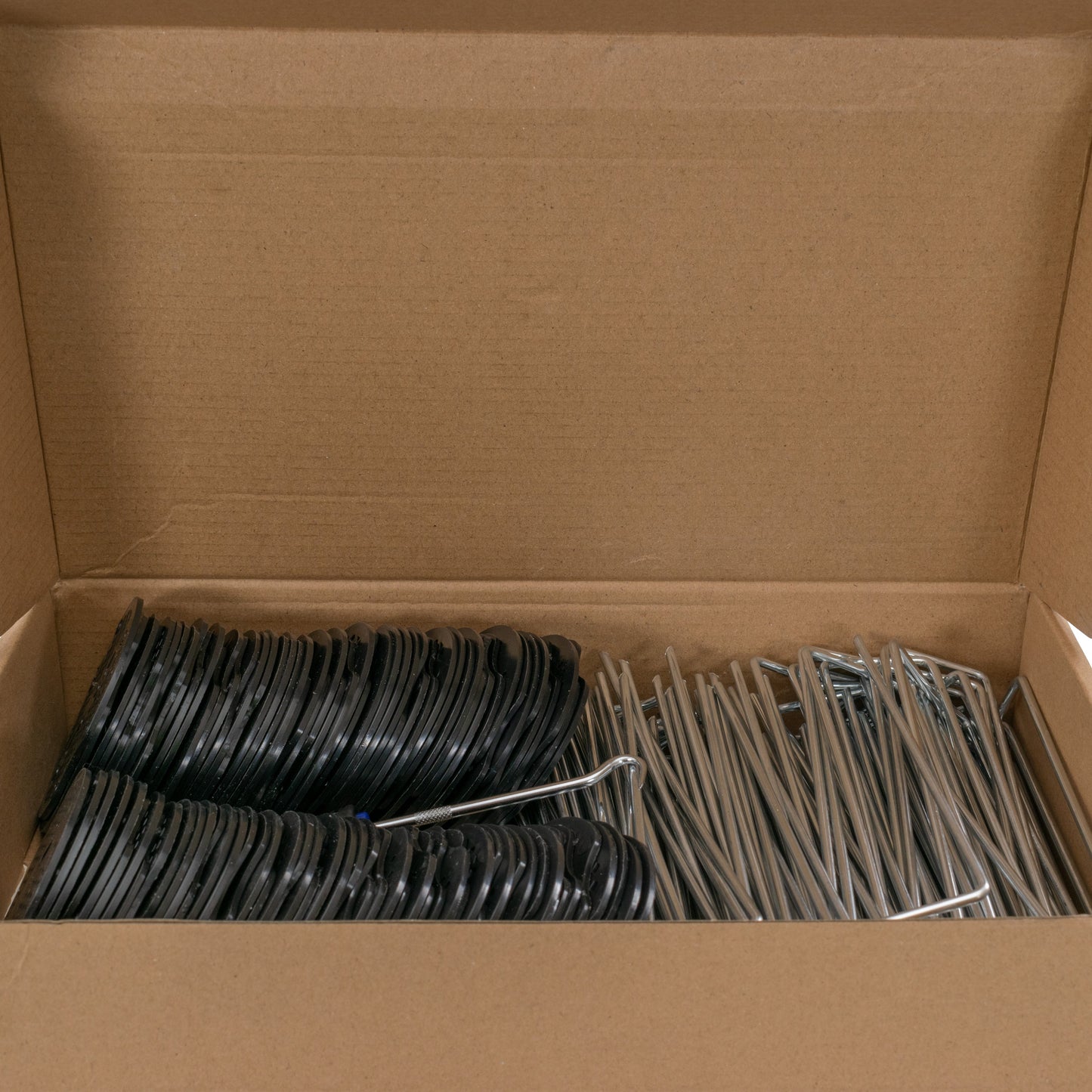 Weed control membrane peg kit in cardboard box with black bases and silver stakes