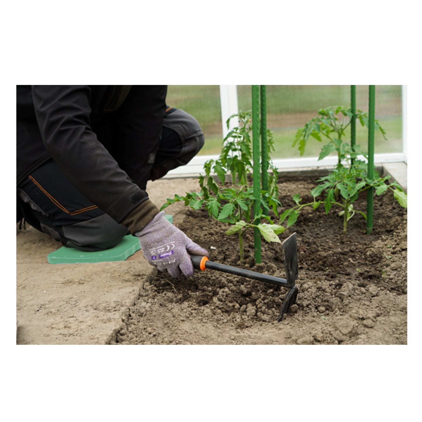 Green kneeler mat with digging hoe in soil while planting