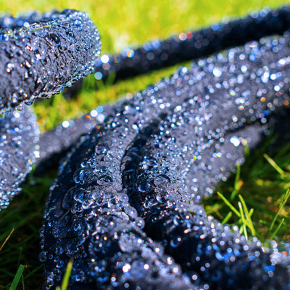 Black porous soaker hose spraying/oozing water, droplets sparkling on grass