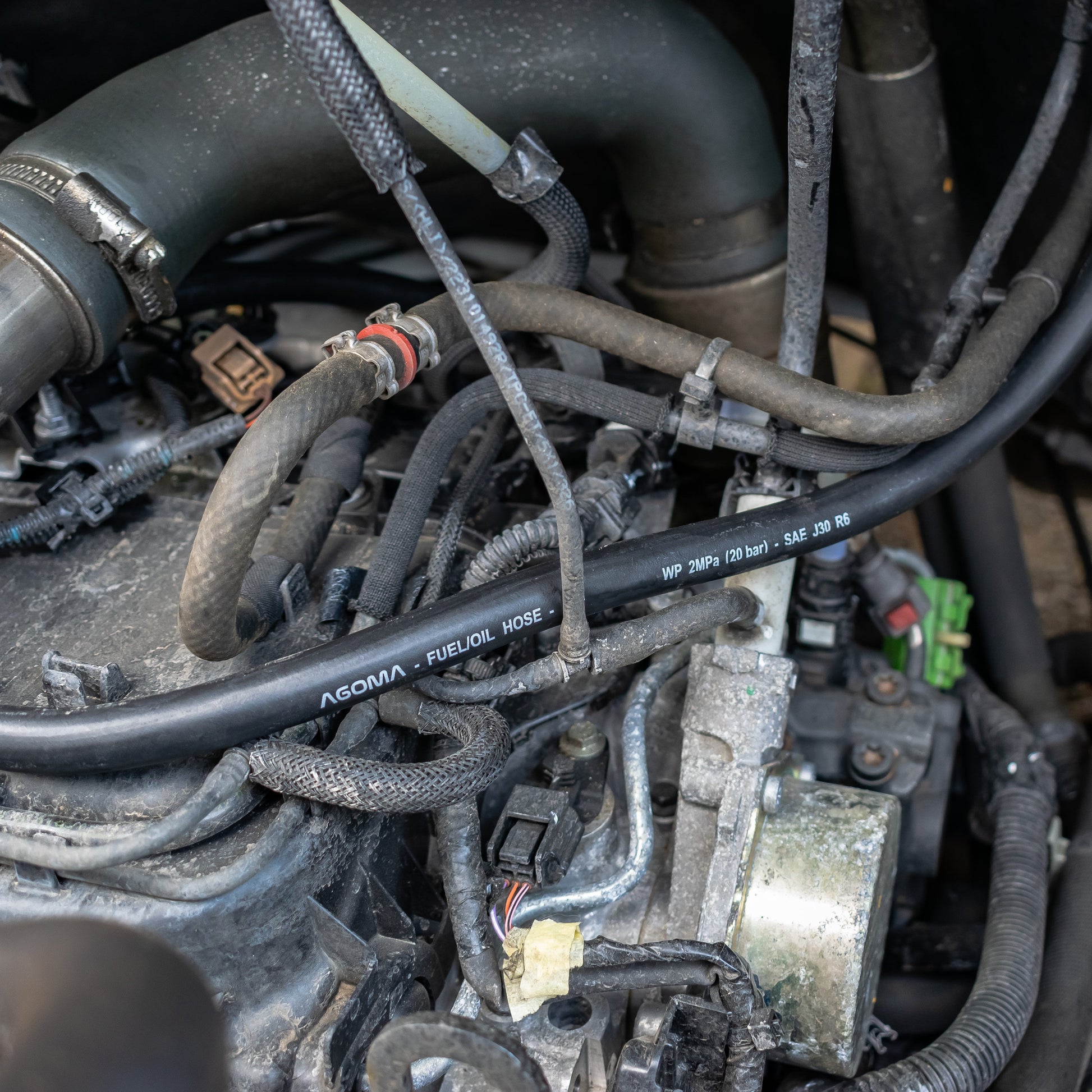 Fuel/oil hose with SAE J30 R6 text installed, black braided hose line in engine bay