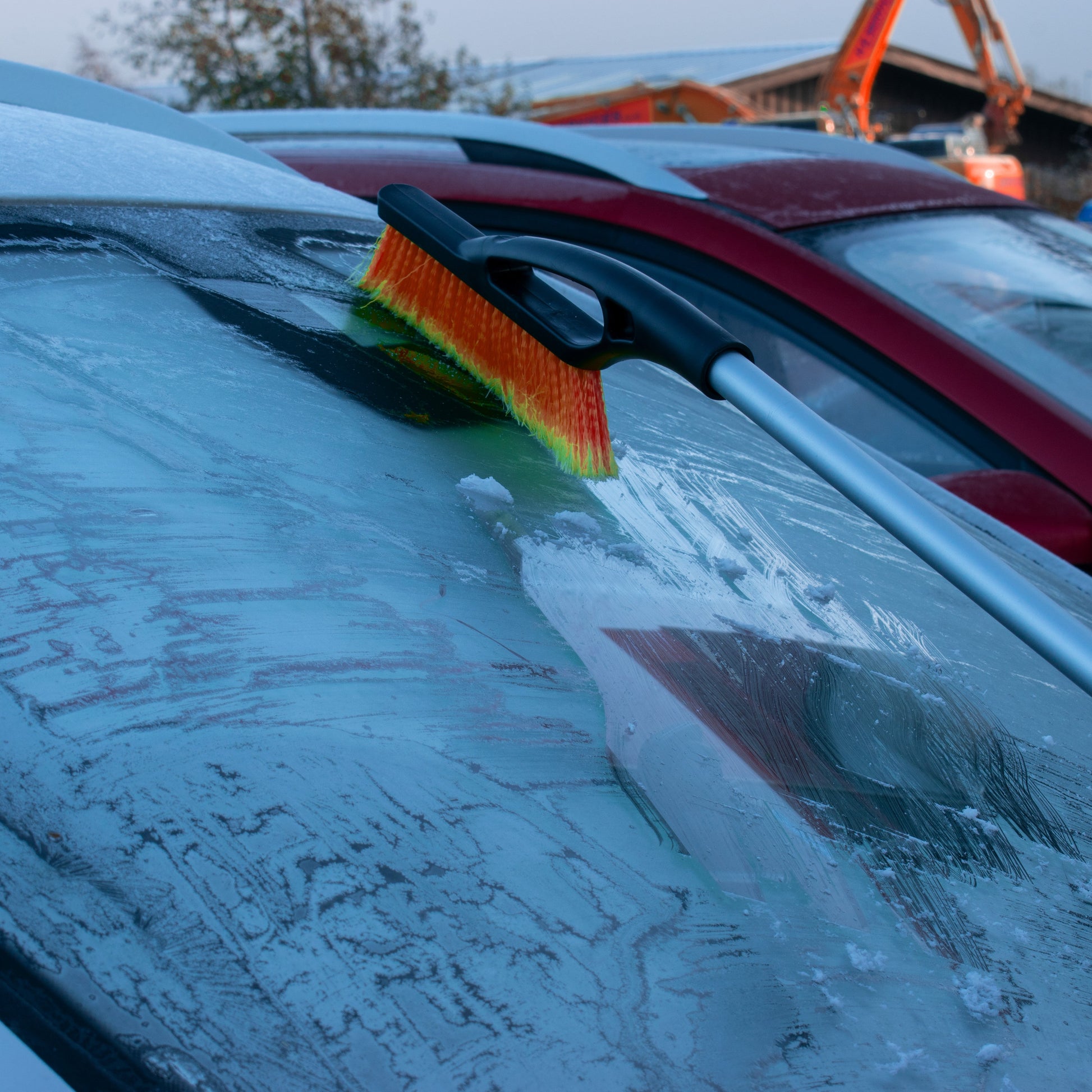Telescopic snow brush with orange bristles clearing snow from a windscreen