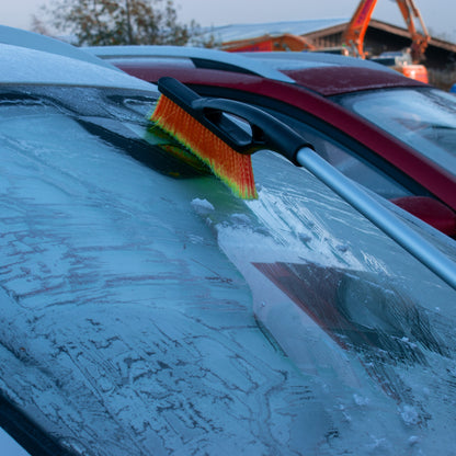 Telescopic snow brush with orange bristles clearing snow from a windscreen