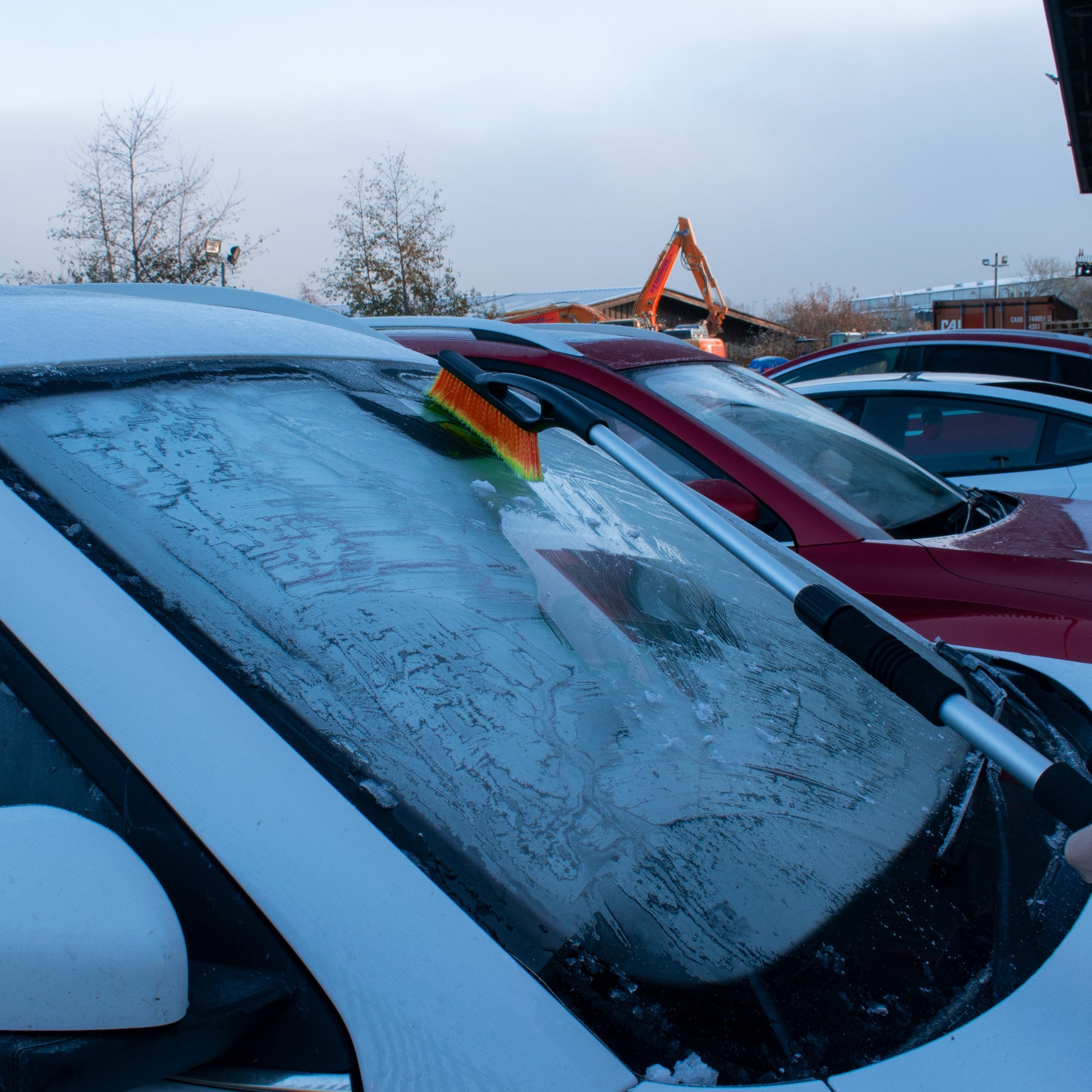 Telescopic snow brush with orange bristle head scraping snow off a windscreen