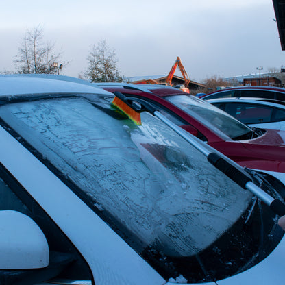 Telescopic snow brush with orange bristle head scraping snow off a windscreen