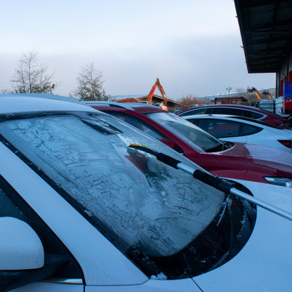 Telescopic snow brush extending across a windscreen, orange bristles in use