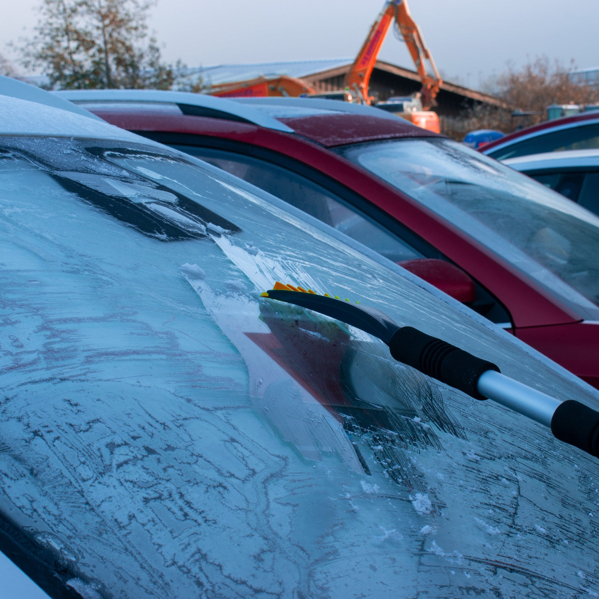 Telescopic snow brush with orange bristles removing frost and snow from glass