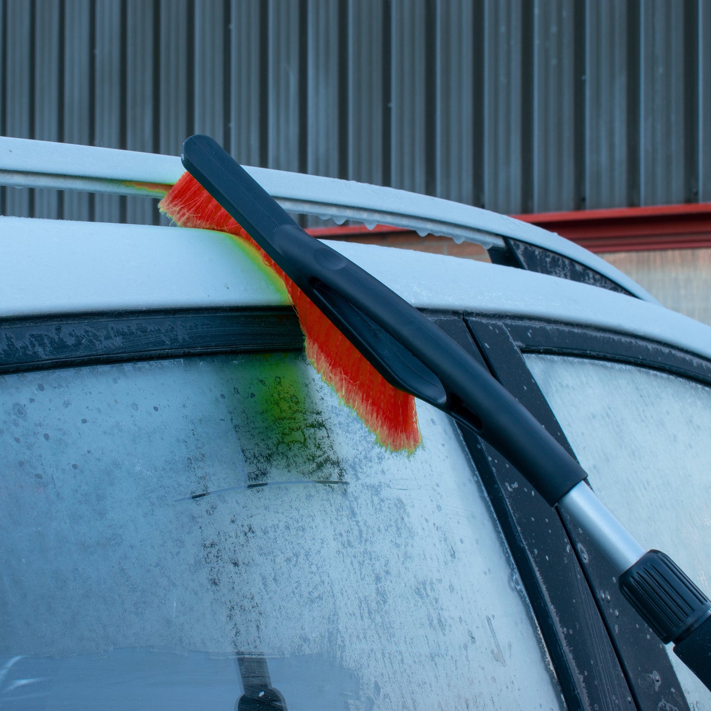 Orange snow brush head scrubbing frosted windshield during winter cleaning