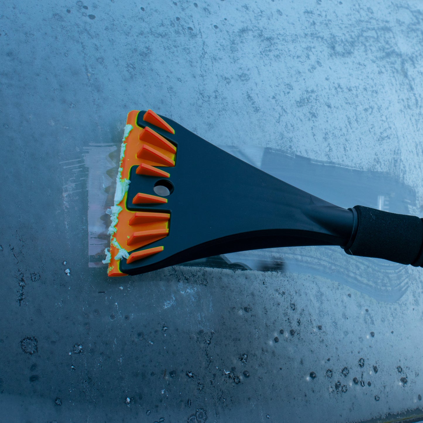 Orange bristle snow brush and scraper blade clearing frost from car window