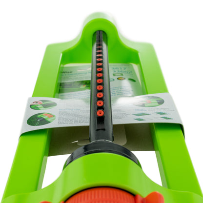 Oscillating sprinkler top view with black tube, rows of red openings, green frame