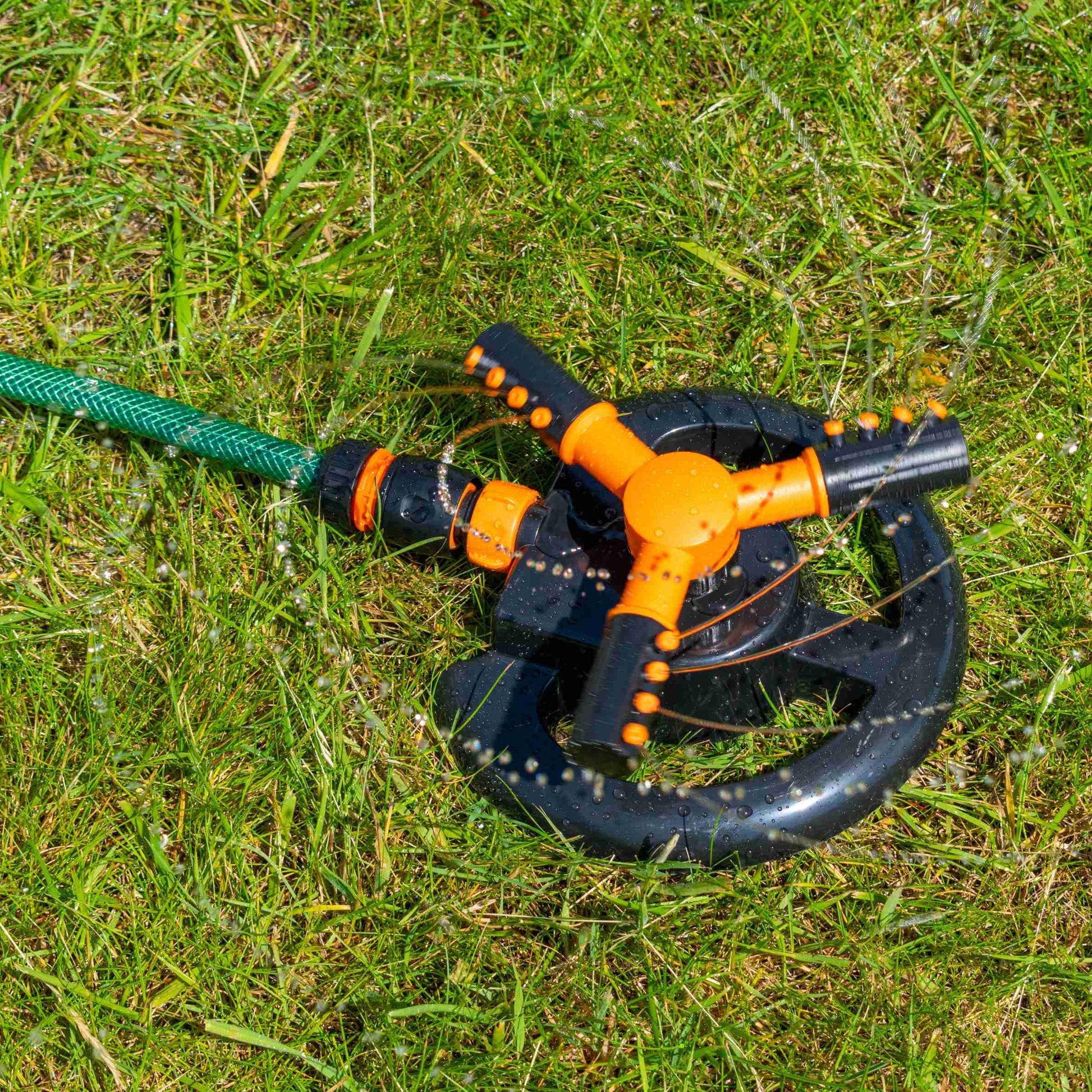 3-Arm Rotationssprinkler, schwarz-oranges Design mit Sprühkopf auf Gras