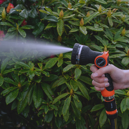 Fan spray from orange-and-black hose sprayer; hand holding handle