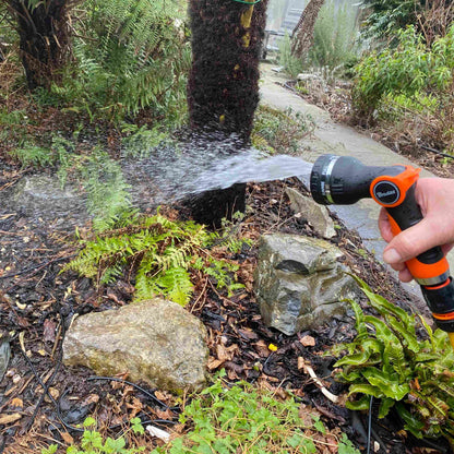 Hose sprayer gun spraying water over ground and rocks; orange nozzle
