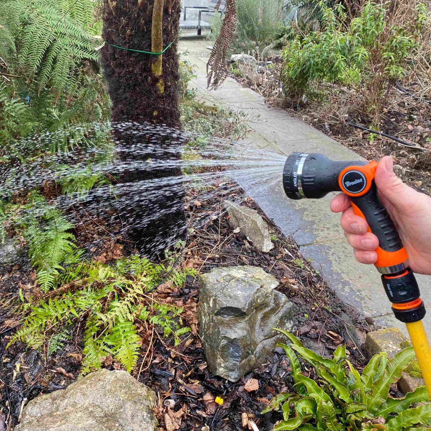 Water sprayer gun spraying stream onto stones; black-and-orange handle