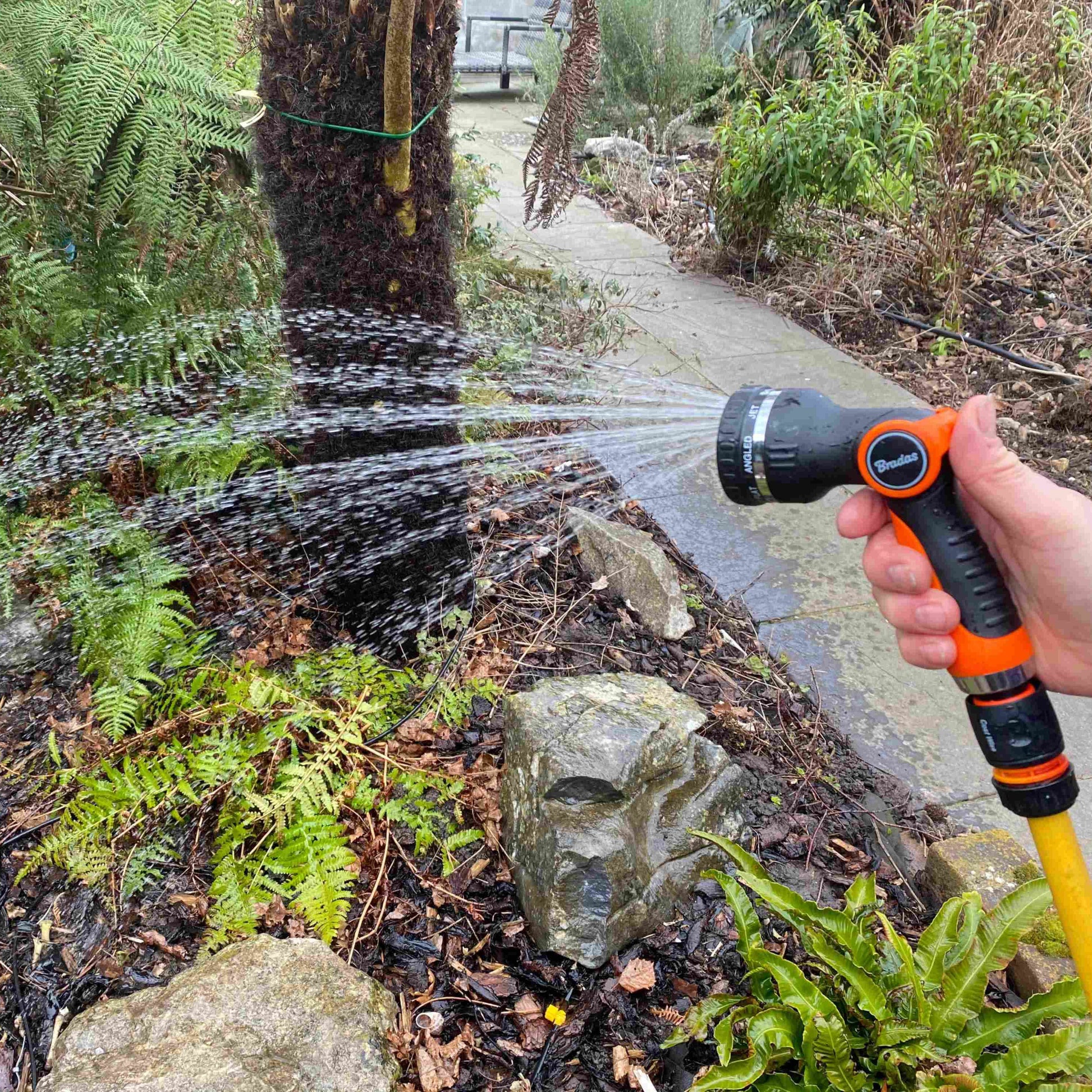 Water sprayer gun spraying stream onto stones; black-and-orange handle