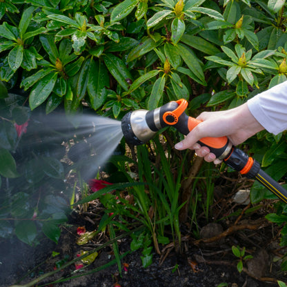 Orange and black hose sprayer gun spraying water over the ground area