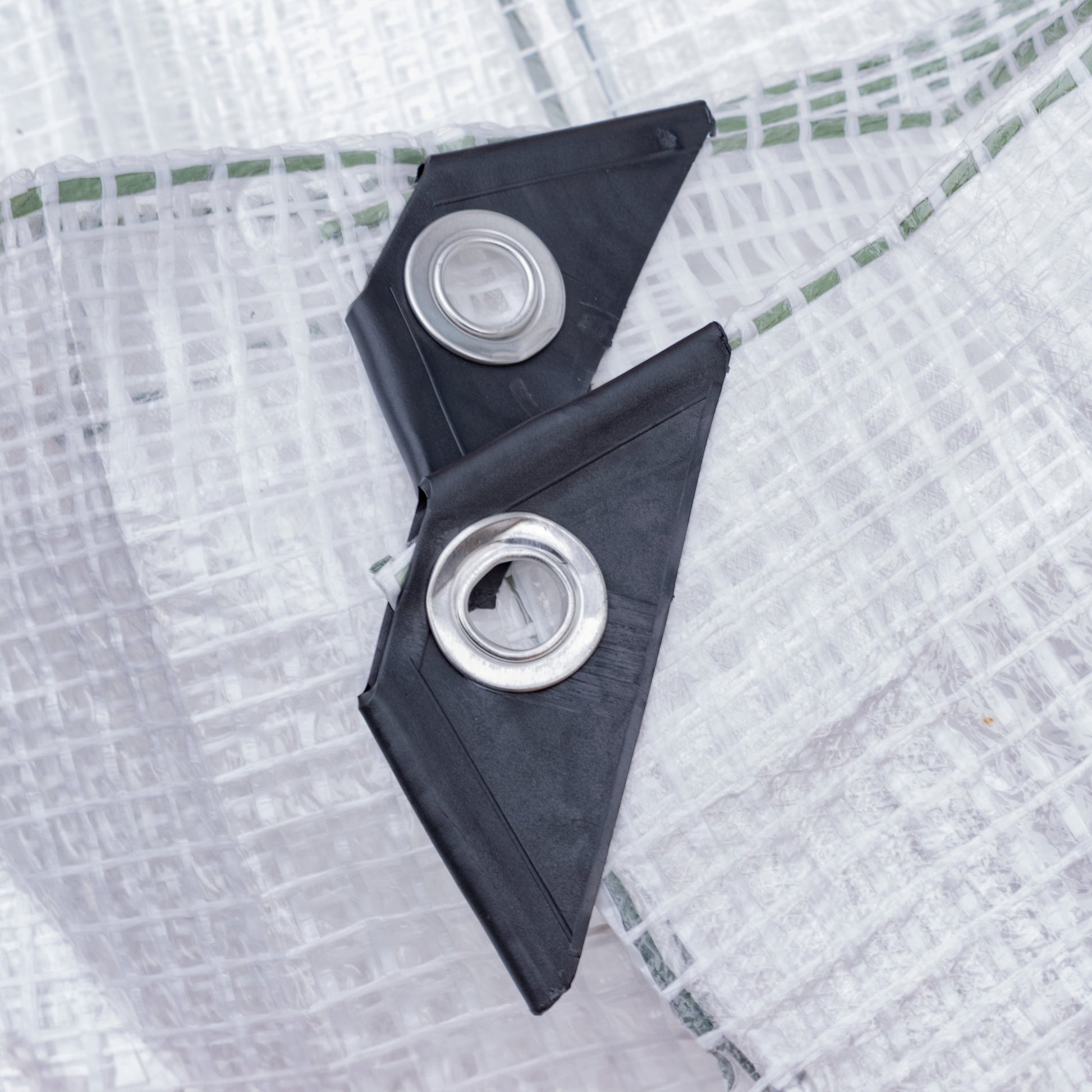 Clear tarpaulin corner close-up, two metal eyelets on black triangular patches