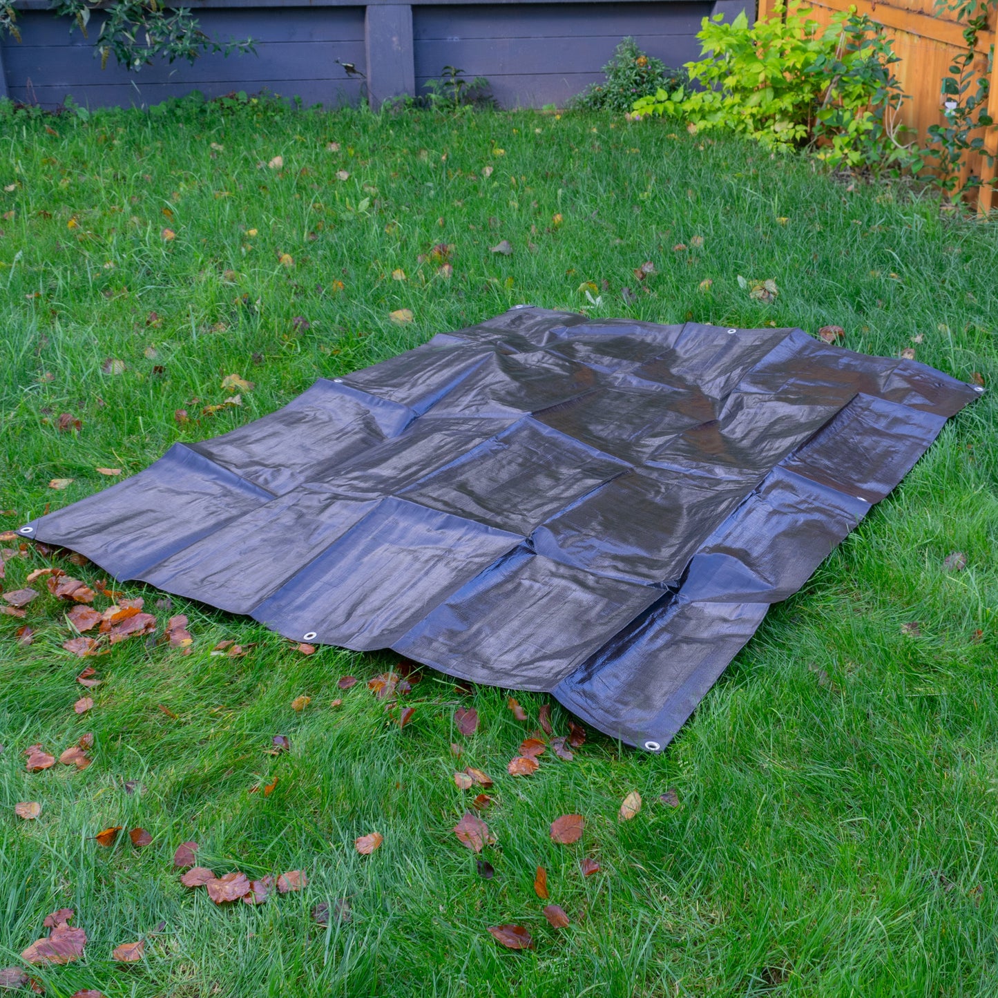 Black tarpaulin sheet laid flat outdoors with corner grommets visible