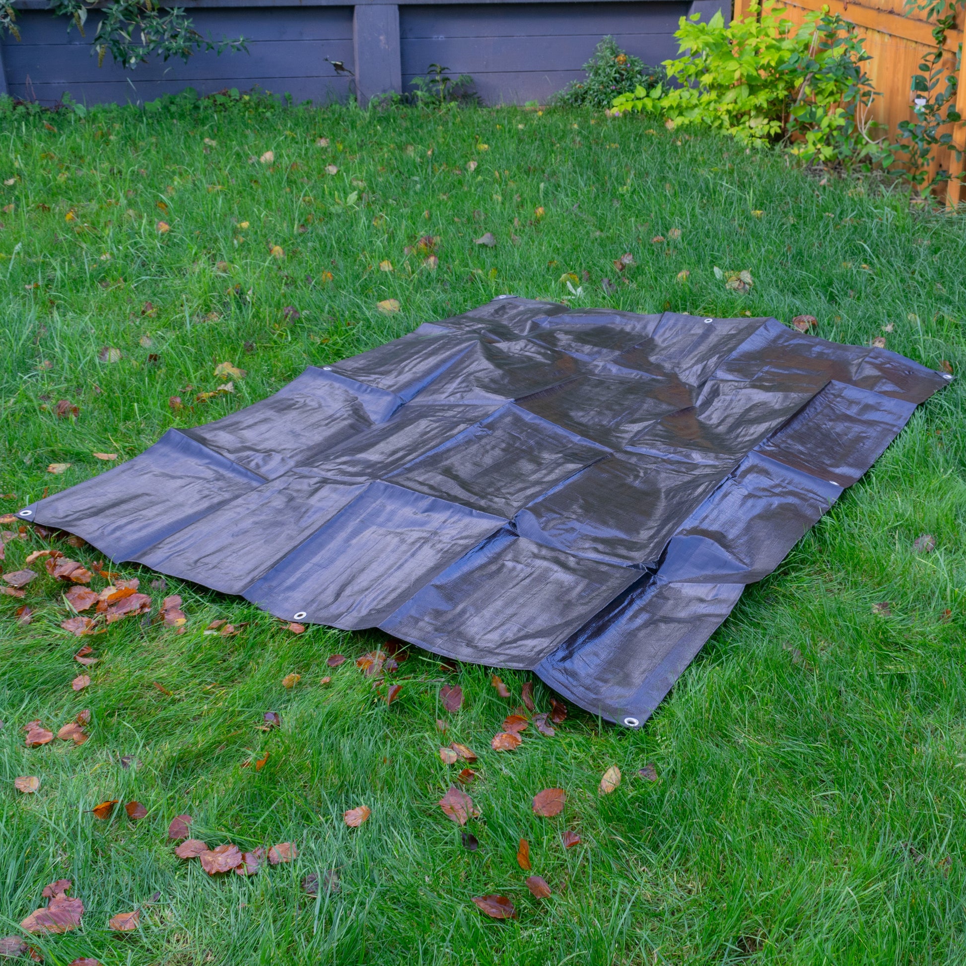 Black tarpaulin sheet laid flat outdoors with corner grommets visible