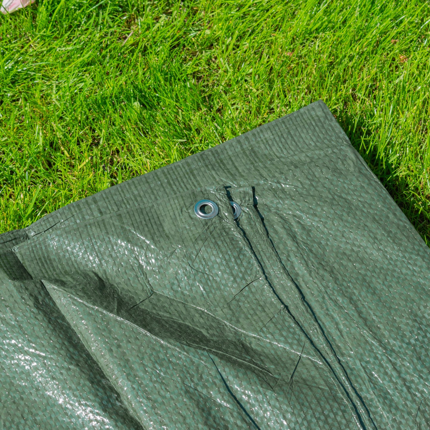 Green tarpaulin close-up of grommet and stitched seam along the edge