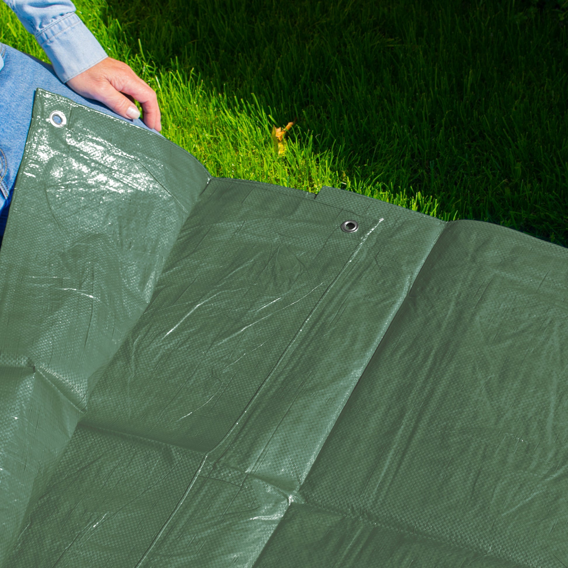 Folded green tarpaulin sheet with metal eyelets for fastening