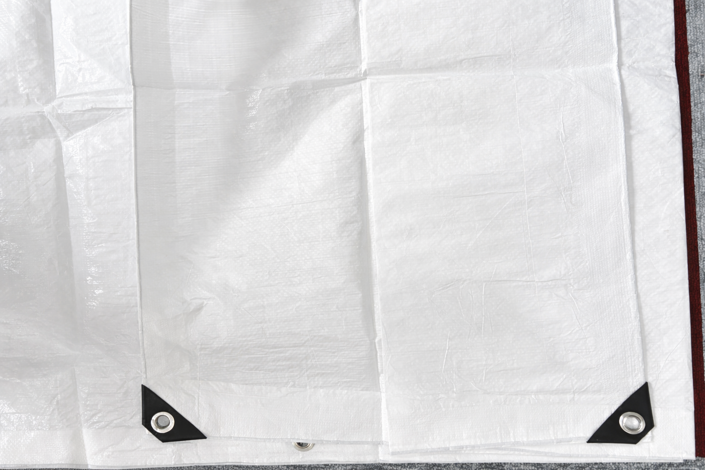 White tarpaulin sheet with black corner patches and metal grommets