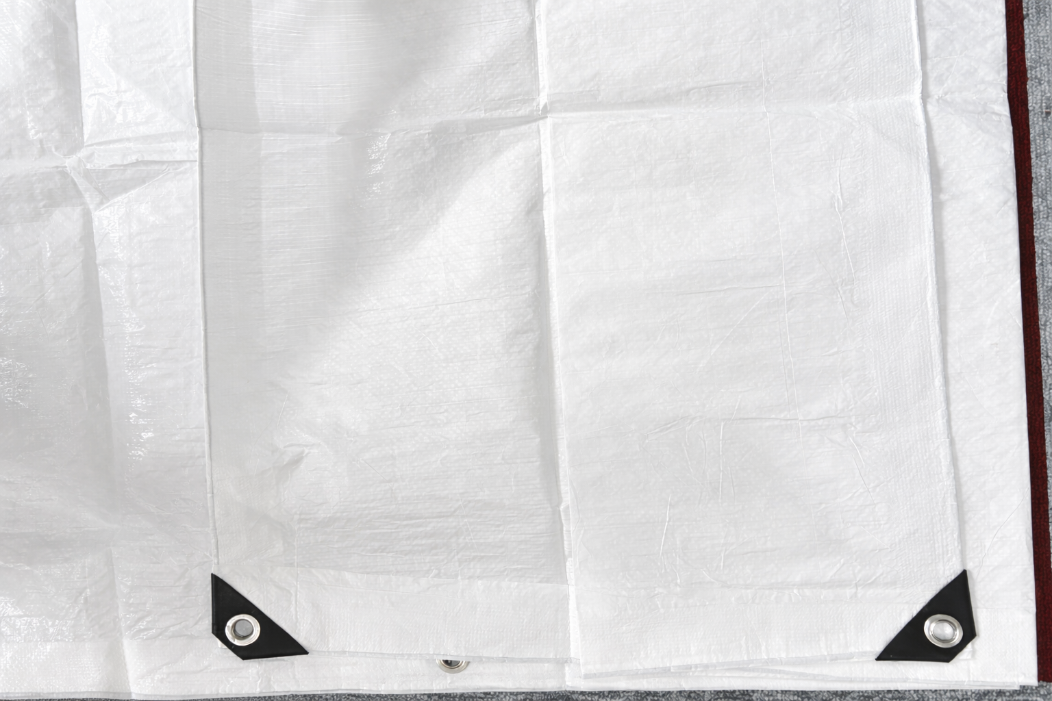 White tarpaulin sheet with black corner patches and metal grommets