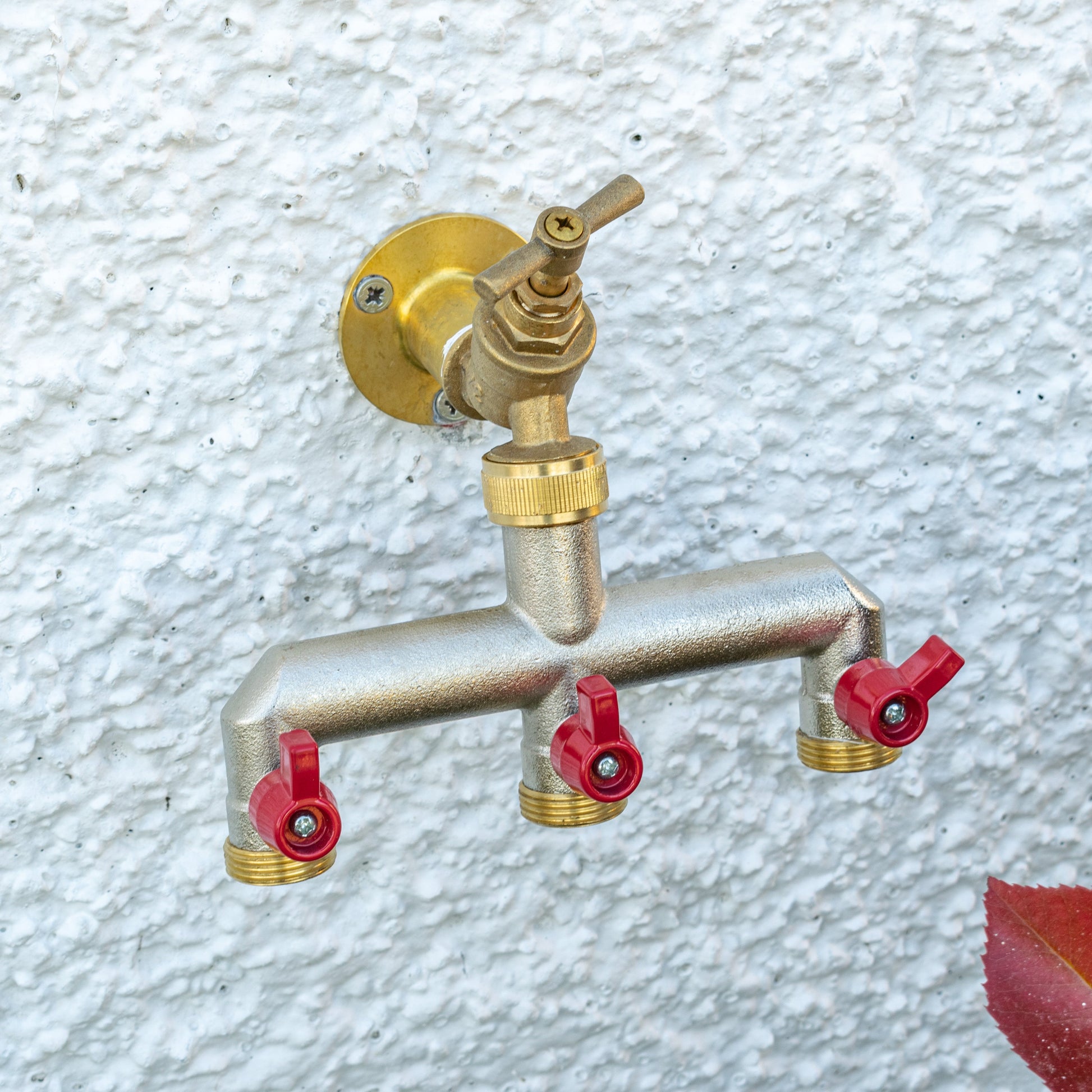 Wall-mounted brass three-way tap splitter with three red shutoff caps and threaded ports