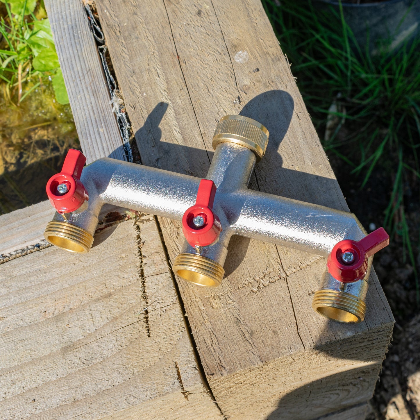 Three-way brass tap splitter with three 3/4" BSP hose connectors and red shutoff caps
