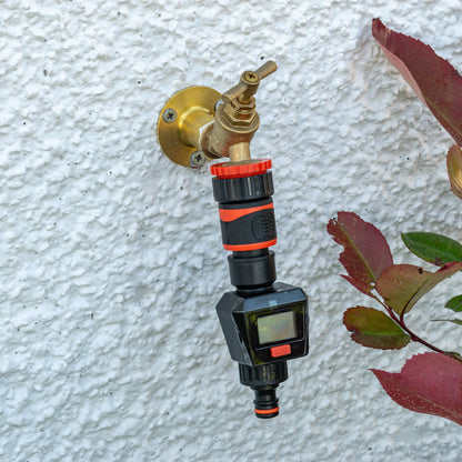 Water flow meter black/orange connected to a brass wall fitting; LCD visible