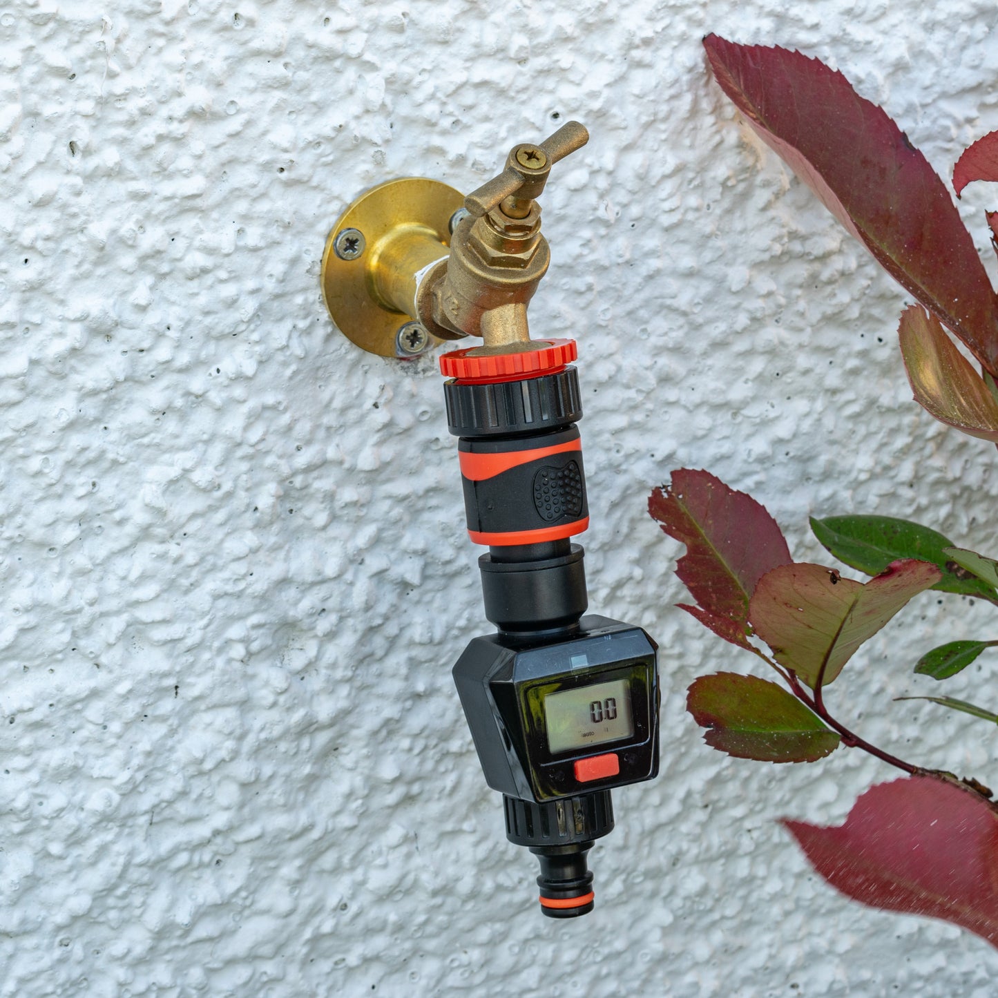 Black/orange water flow meter attached to a brass inlet with LCD display