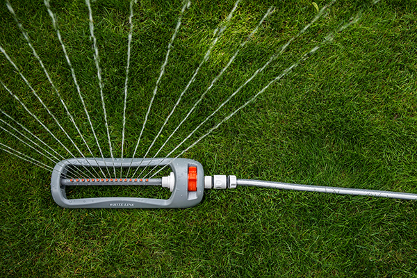 Oscillating sprinkler releasing a fan of water spray over green lawn